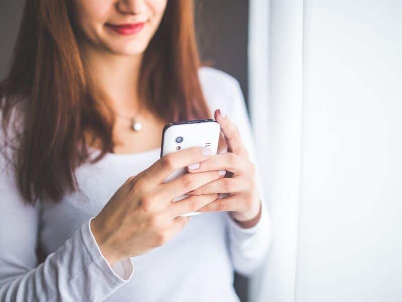 woman smiling while looking at mobile phone
