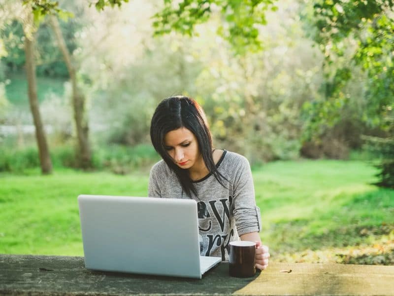 woman using laptop computer outdoors with mug of tea